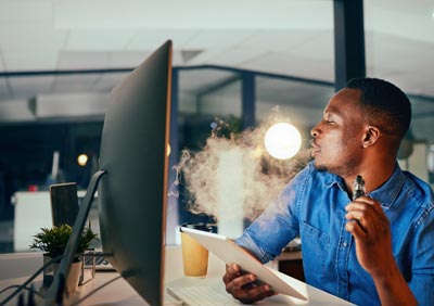 Man-at-work-vaping-e-cigarette-at-his-desk